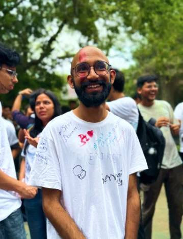 Aniket smiling in a white T-shirt covered in friends' scribbles
